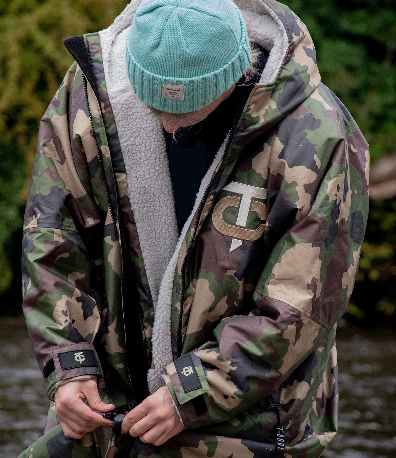 Image of a man zipping up his camo and grey T-Robe outdoors