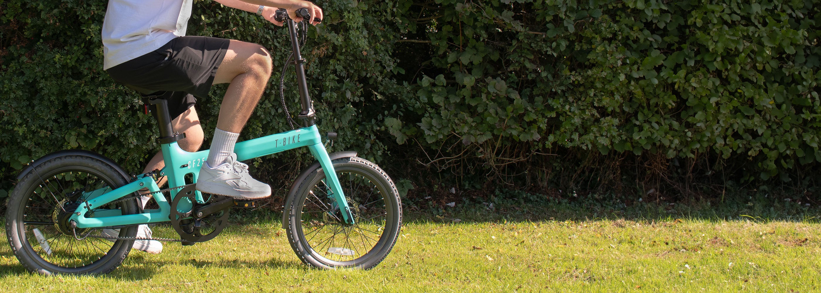 Image of the CF250 Folding carbon fibre E-Bike in turquoise being ridden on grass