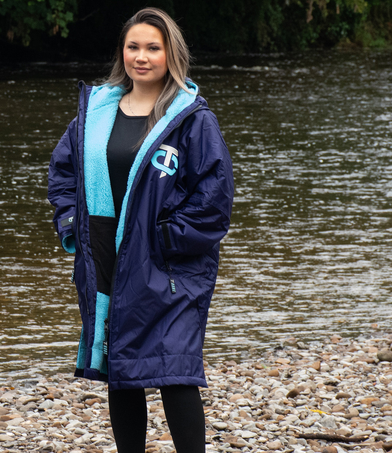 Image of a woman wearing a deep purple and blue weatherproof poncho by a river 